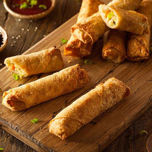 Spring rolls over wooden tray with bowls of hot chili sauce and soy sauce